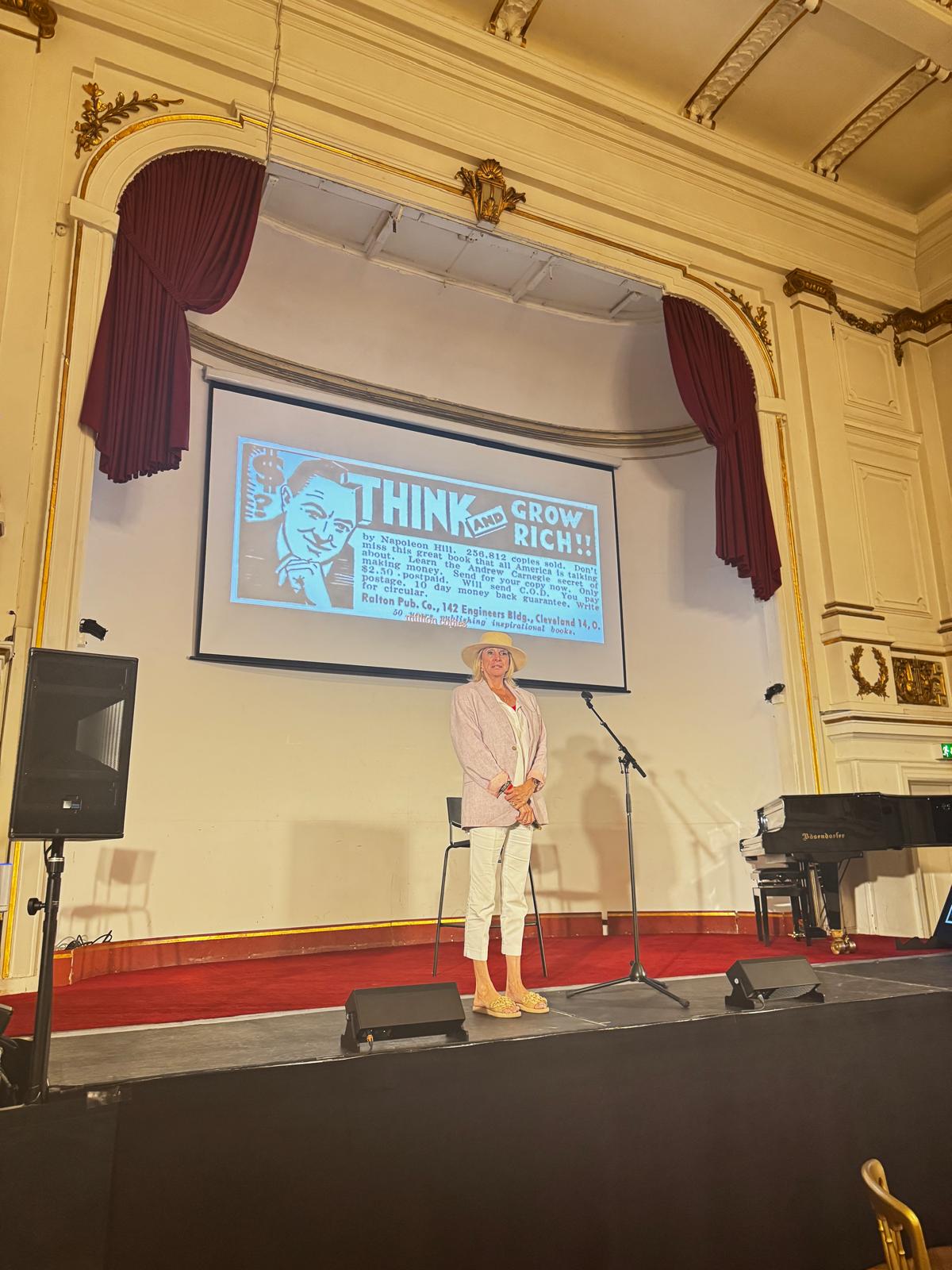 Speaker on stage beside a historic Think and Grow Rich advertisement