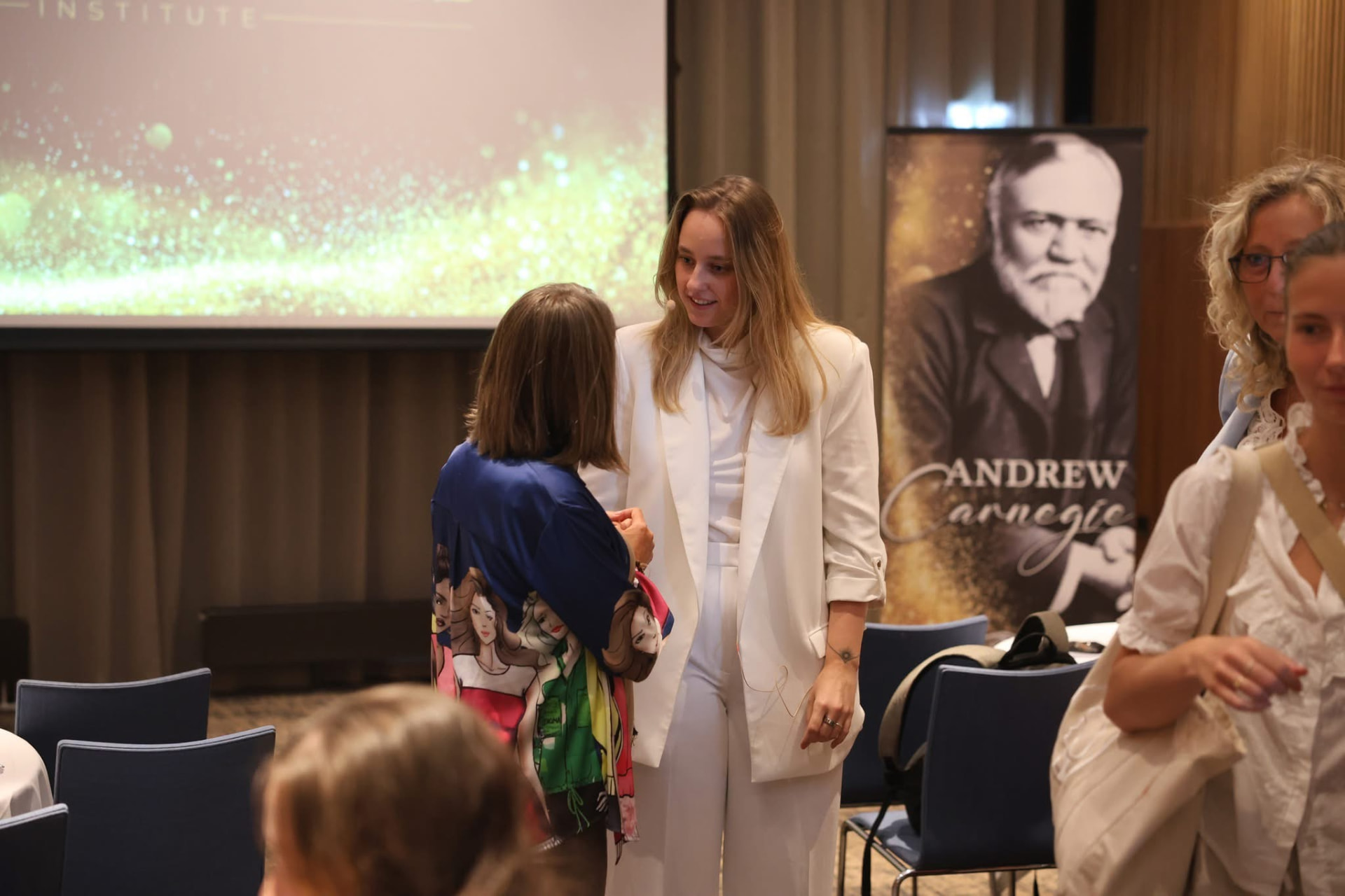 Host welcoming a guest beside an Andrew Carnegie banner at an Institute event
